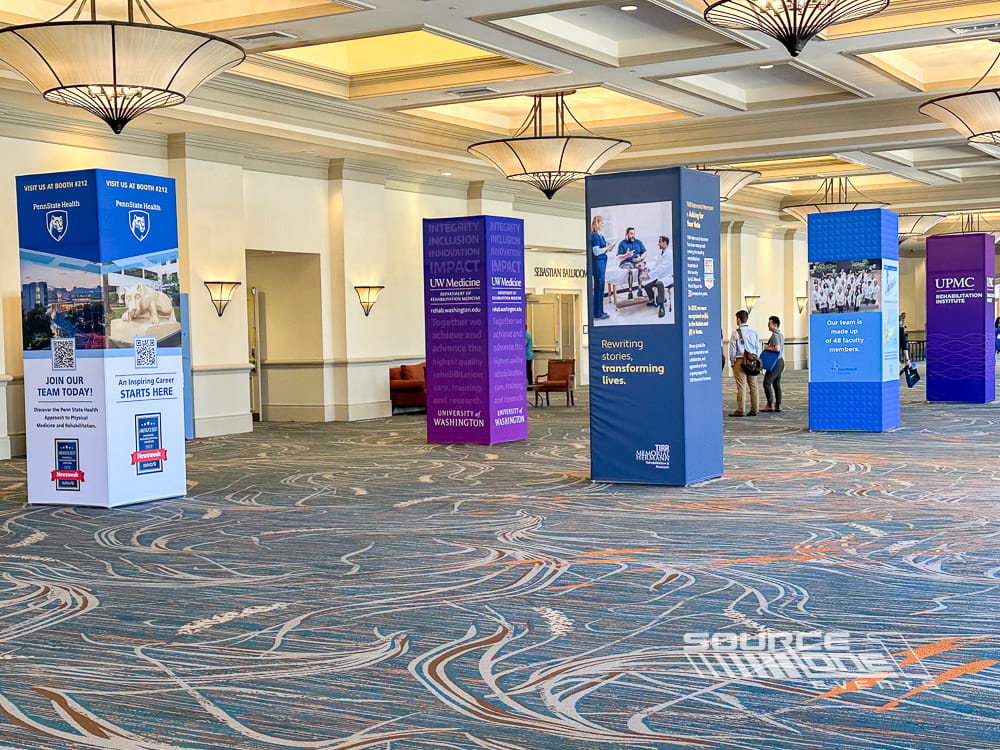 Modern conference information tower wrapped in vibrant blue graphics and sponsor branding.
