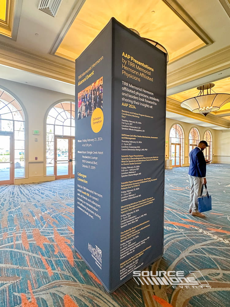 Tall freestanding branded tower with bold blue graphics providing conference information and attendee navigation.