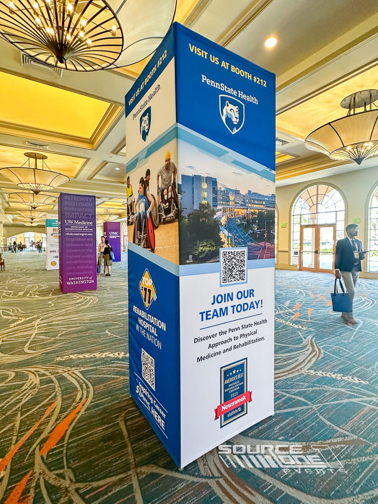 Fabric-wrapped architectural column featuring blue and gold conference branding inside a hotel convention center.