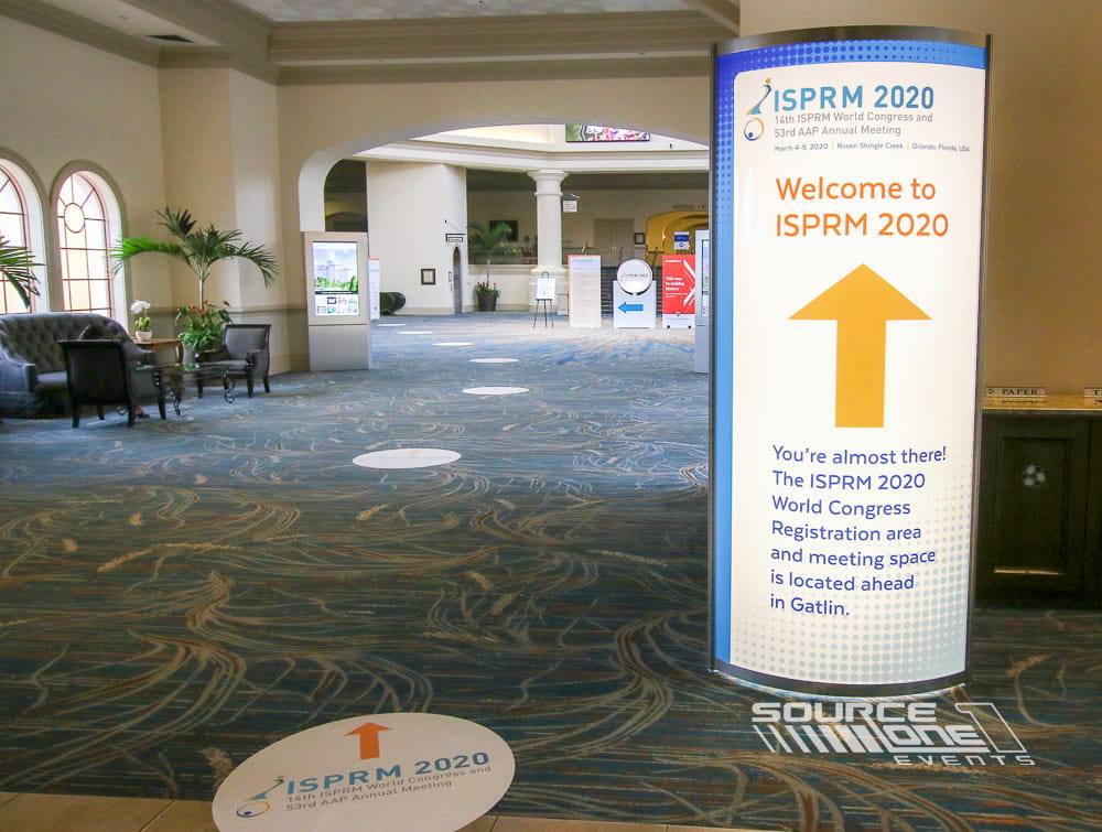 Purple illuminated backlit tower with white conference graphics providing attendee wayfinding and sponsor visibility.