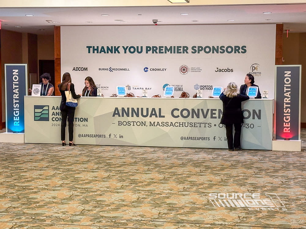 Large registration area with sponsor backdrop, attendee service counters, and branded conference welcome graphics.