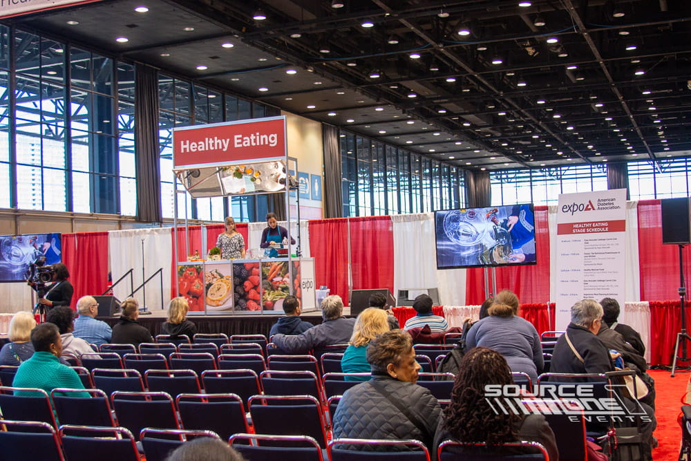 Healthy Living educational stage with green branded graphics, presentation seating, and attendee learning environment.
