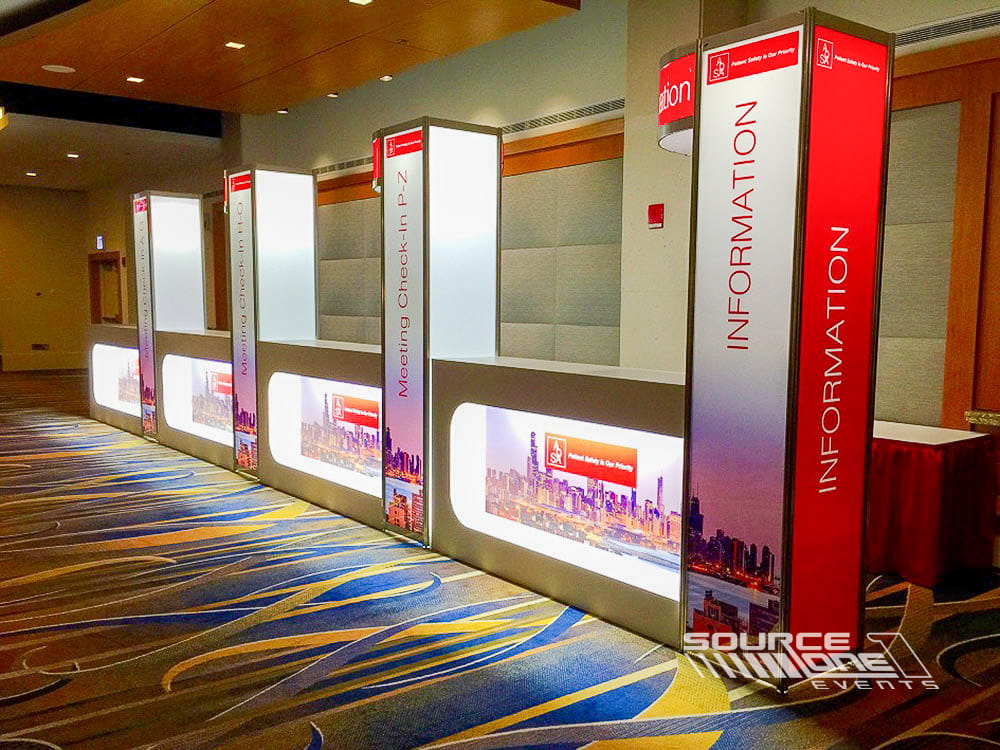 Custom registration counters featuring red and white side panel graphics, attendee check-in stations, and organized registration layout.