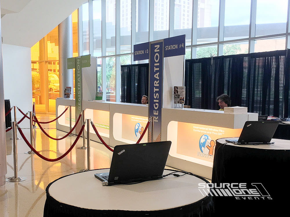 Custom registration counters with blue side panels, branded graphics, and attendee welcome stations inside a convention center.
