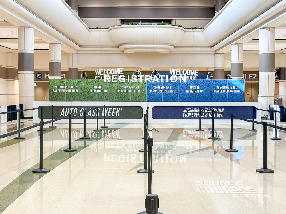 Wide conference registration area featuring green branded backdrop, attendee queuing lanes, and organized check-in counters.