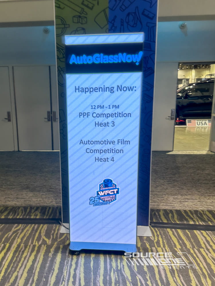 Freestanding LED digital poster showcasing event schedule and branded conference messaging within the exhibit hall.