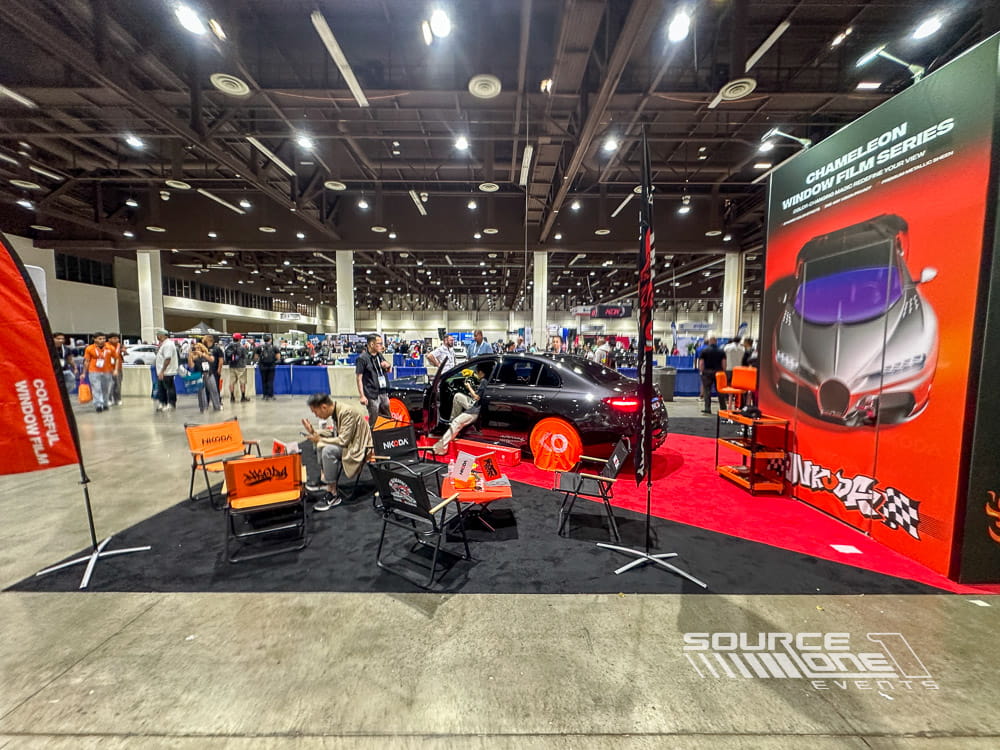 Large island exhibit showcasing bold red and black graphics, suspended signage, product displays, and attendee engagement on the trade show floor.