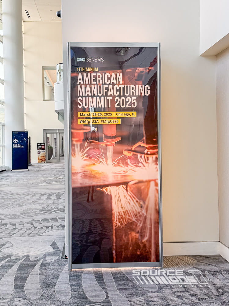 Large illuminated backlit tower with bold event branding and vibrant orange graphics positioned in a conference lobby.
