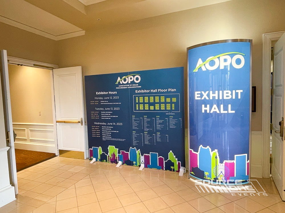 Blue illuminated backlit tower featuring conference branding and directional graphics leading attendees to the exhibit hall.