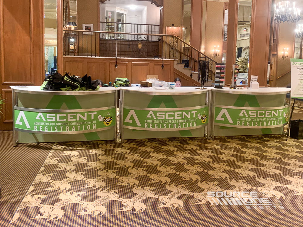 Green branded registration counters with custom graphics, attendee service desks, and elegant hotel convention center backdrop.