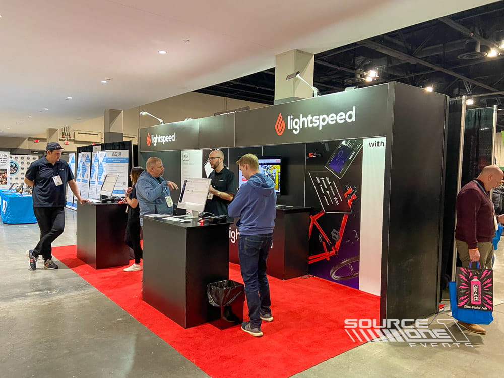 Custom trade show booth for Lightspeed featuring illuminated branding, product displays, digital technology, and welcoming exhibitor meeting space.