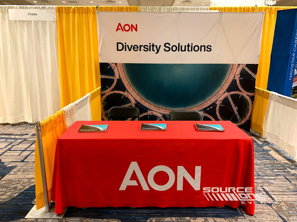 AON-branded promotional table with custom fabric table cover, bold corporate graphics, and exhibitor marketing display.