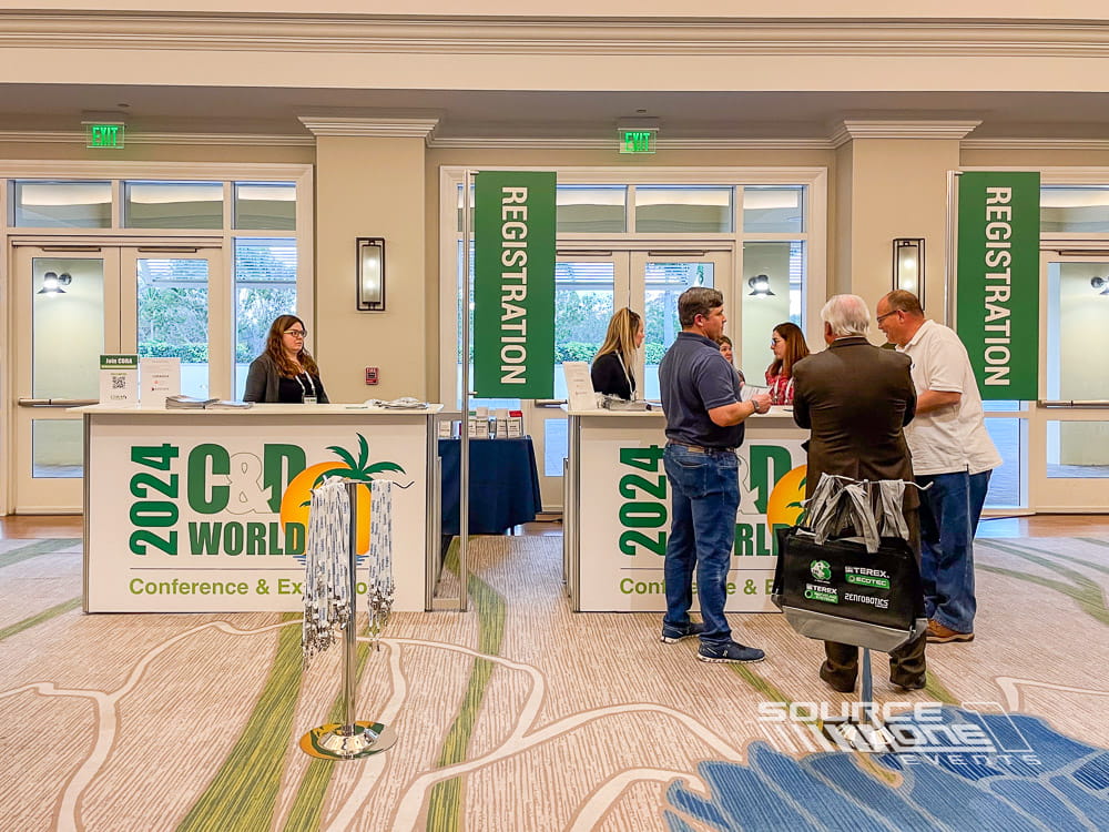 Contemporary registration counters with black and teal branded graphics, attendee check-in stations, and digital information displays.