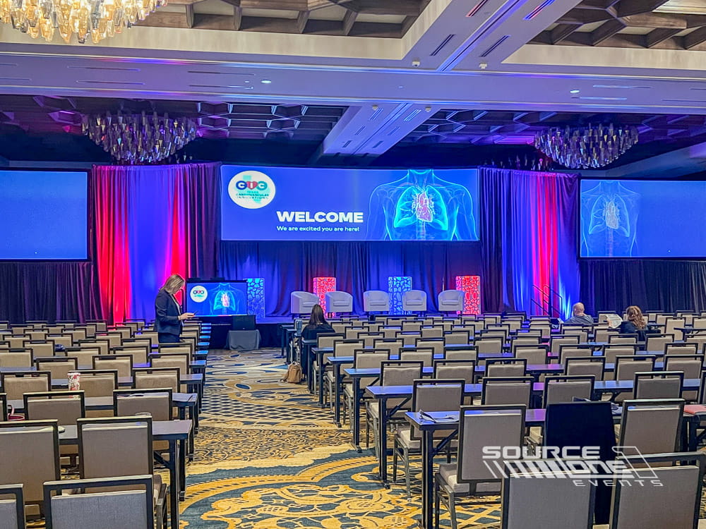 Contemporary conference stage with vibrant LED lighting, branded presentation graphics, and professional audiovisual production.