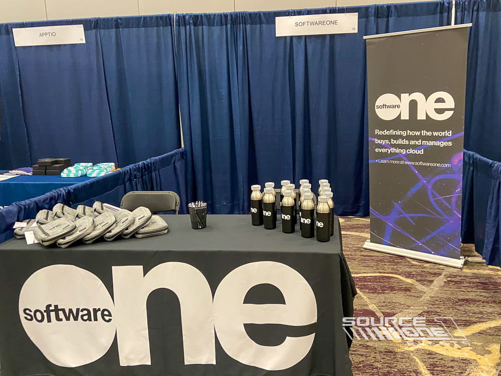 Custom branded exhibit table with navy blue table throw, promotional materials, and attendee engagement area at a technology conference, produced by Source One Events.