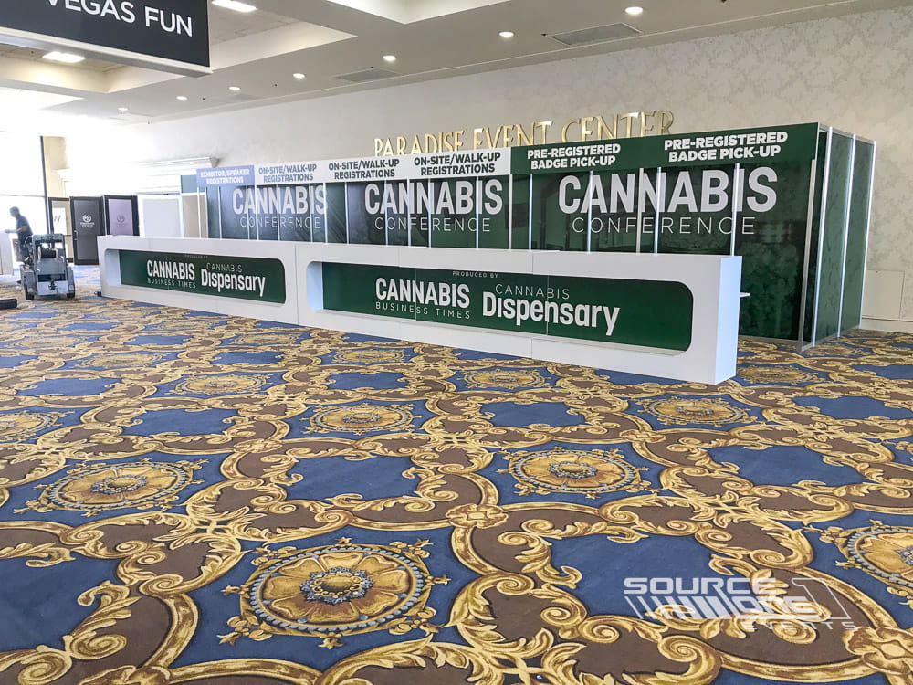 Large custom registration desk featuring bold green Cannabis Conference branding, attendee service counters, and convention center wayfinding.