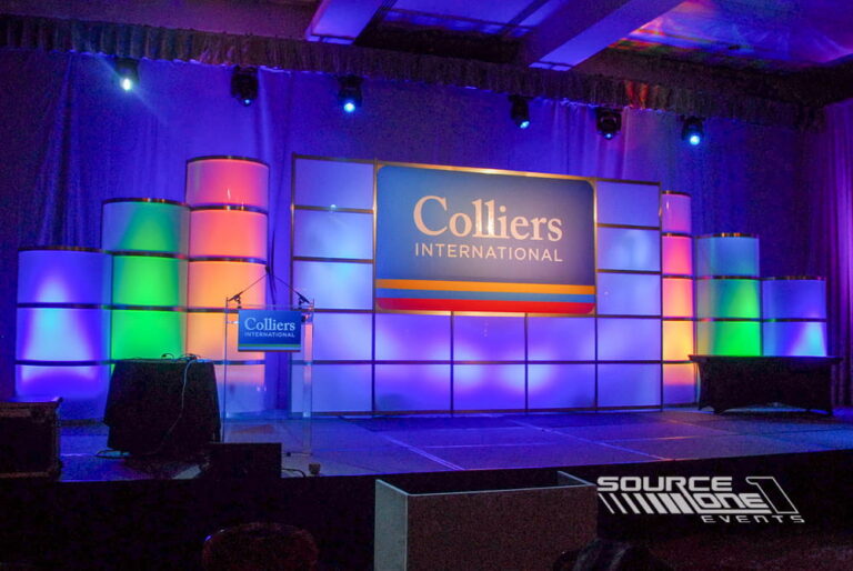 Corporate conference stage with blue and purple uplighting, branded backdrop, and keynote presentation setup.