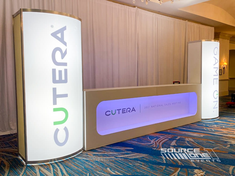 Elegant registration counter featuring purple branded graphics, wood finishes, and digital attendee information displays.