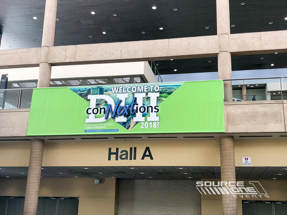 Overhead banner featuring conference branding installed above the exhibit hall entrance.