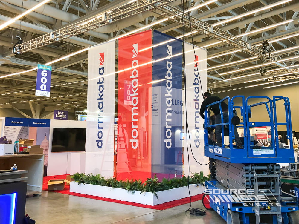 Tall vertical hanging banners with colorful conference graphics suspended above exhibit aisles for attendee wayfinding.