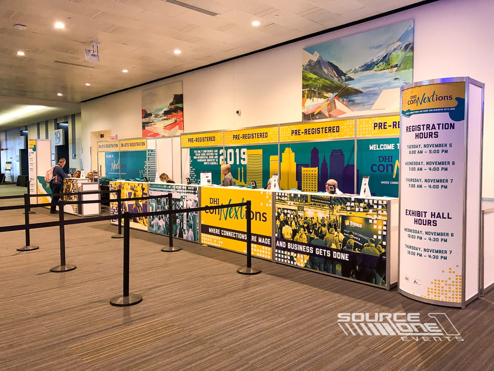 Custom registration counter with colorful sponsor branding, attendee service desks, and organized conference check-in layout.