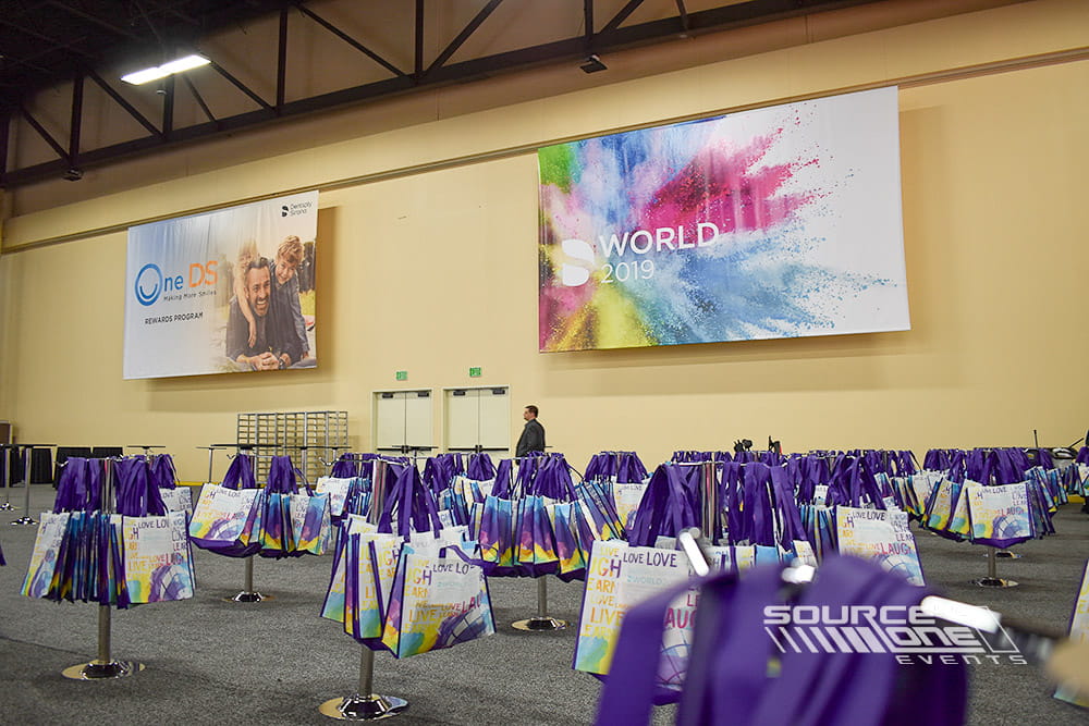 Large suspended conference banner with colorful DS World branding positioned above registration and attendee gathering areas.