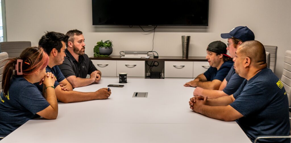 Team meeting around a conference table discussing exhibit production, event logistics, and project planning.