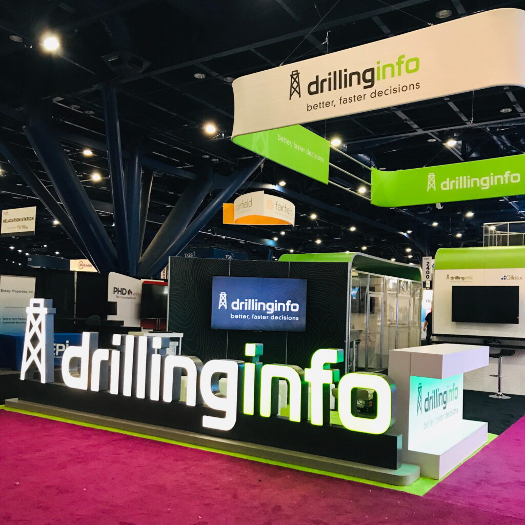 Large custom trade show exhibit with suspended green branding, meeting areas, and technology-driven product displays.