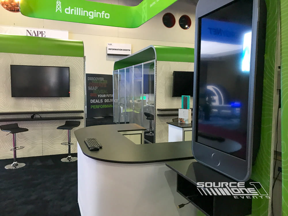 Large custom exhibit featuring green illuminated branding, meeting rooms, product displays, and open attendee interaction areas.