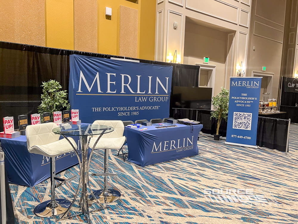 Merlin exhibit featuring branded pop-up display, custom table throw, and attendee information station.