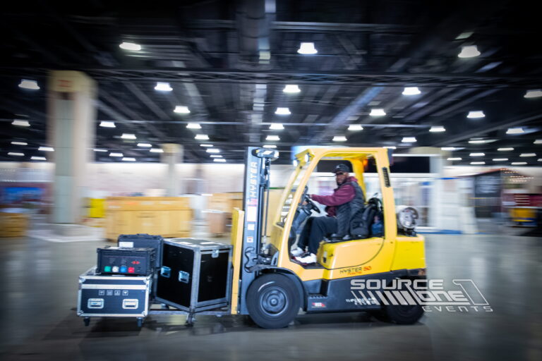 Forklift transporting exhibit materials across a convention center show floor during event setup.