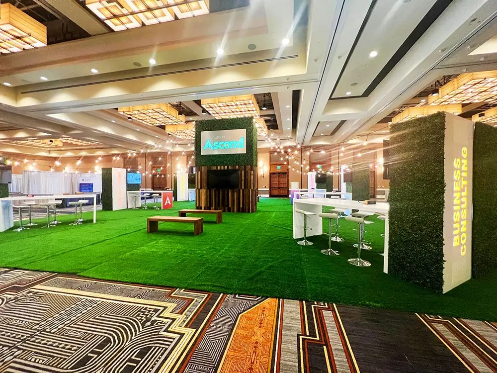 Branded networking lounge with artificial turf, seating, and presentation displays inside a convention center.