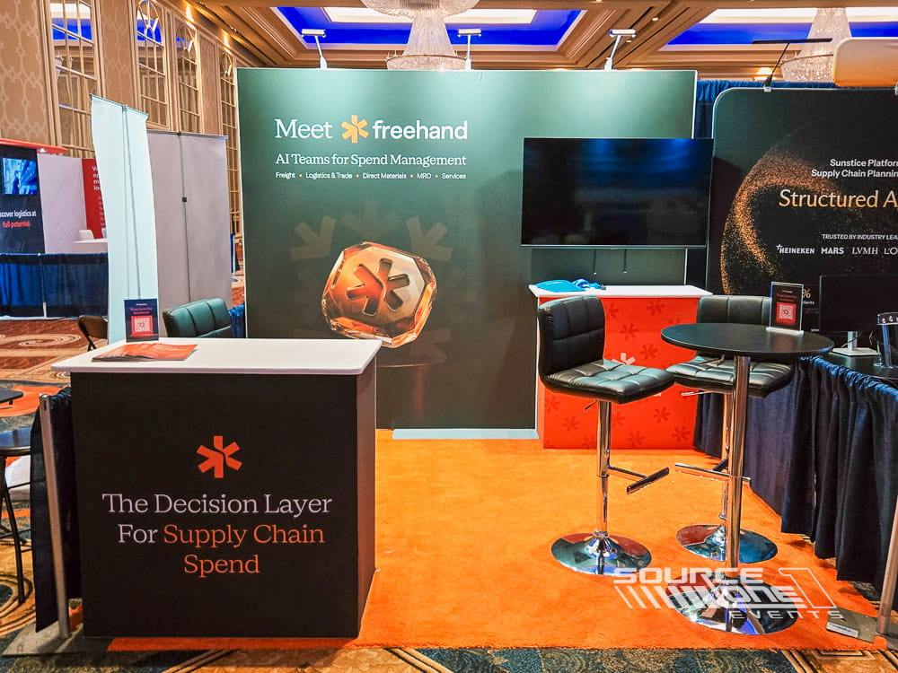 Hospitality-inspired exhibit featuring teal branding, comfortable seating, digital monitor, and premium custom booth design.