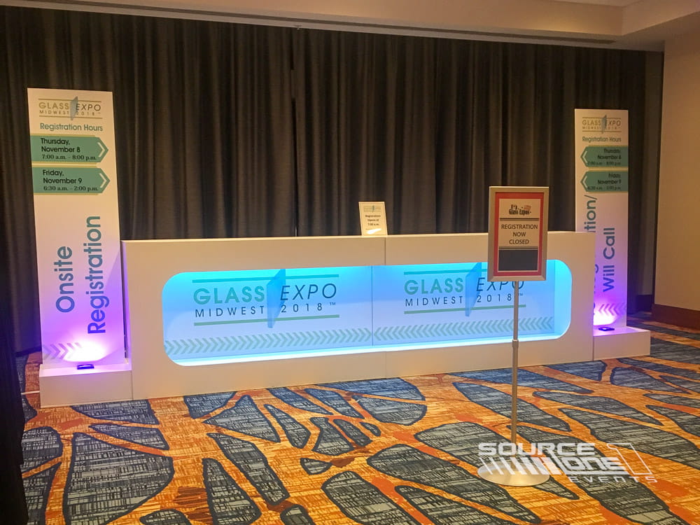 Contemporary registration desk with glowing blue counters, branded graphics, and modern attendee check-in experience.