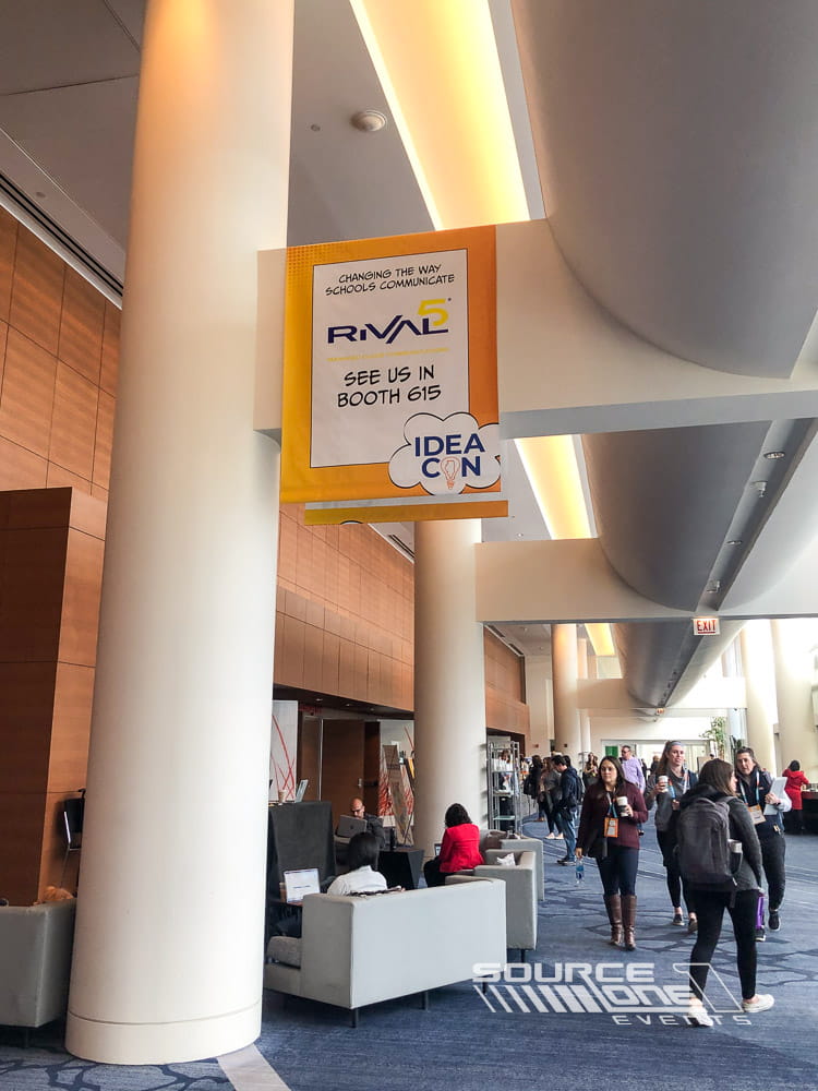 Ceiling-mounted conference banner featuring vibrant event branding and directional messaging inside the exhibit hall.