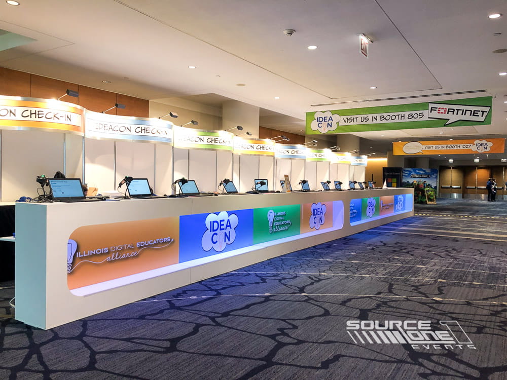 Modern registration counter with blue branded graphics, illuminated check-in stations, and conference attendee services.