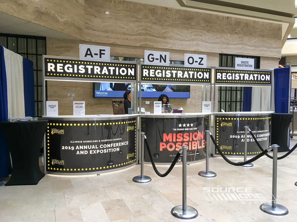 Large registration area featuring overhead alphabetical wayfinding signs, multiple check-in counters, and efficient attendee flow.
