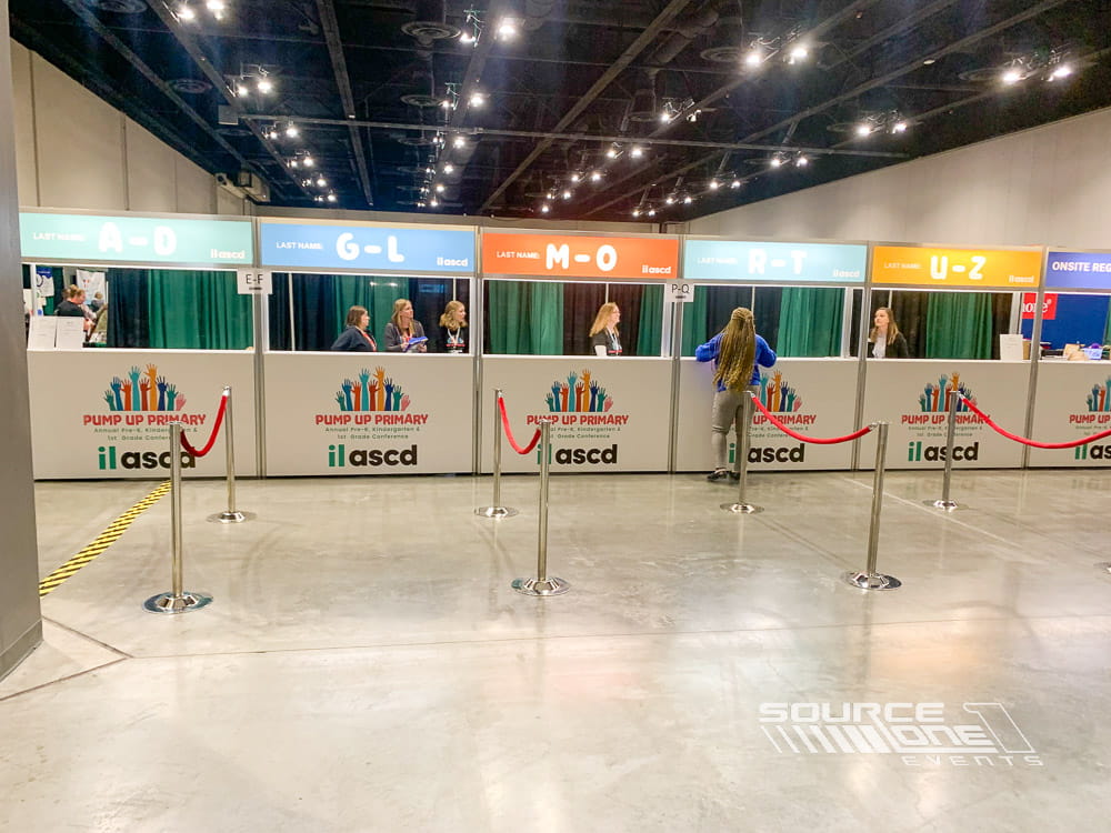 Contemporary registration counter with green and blue branded graphics, digital signage, and organized attendee check-in stations.