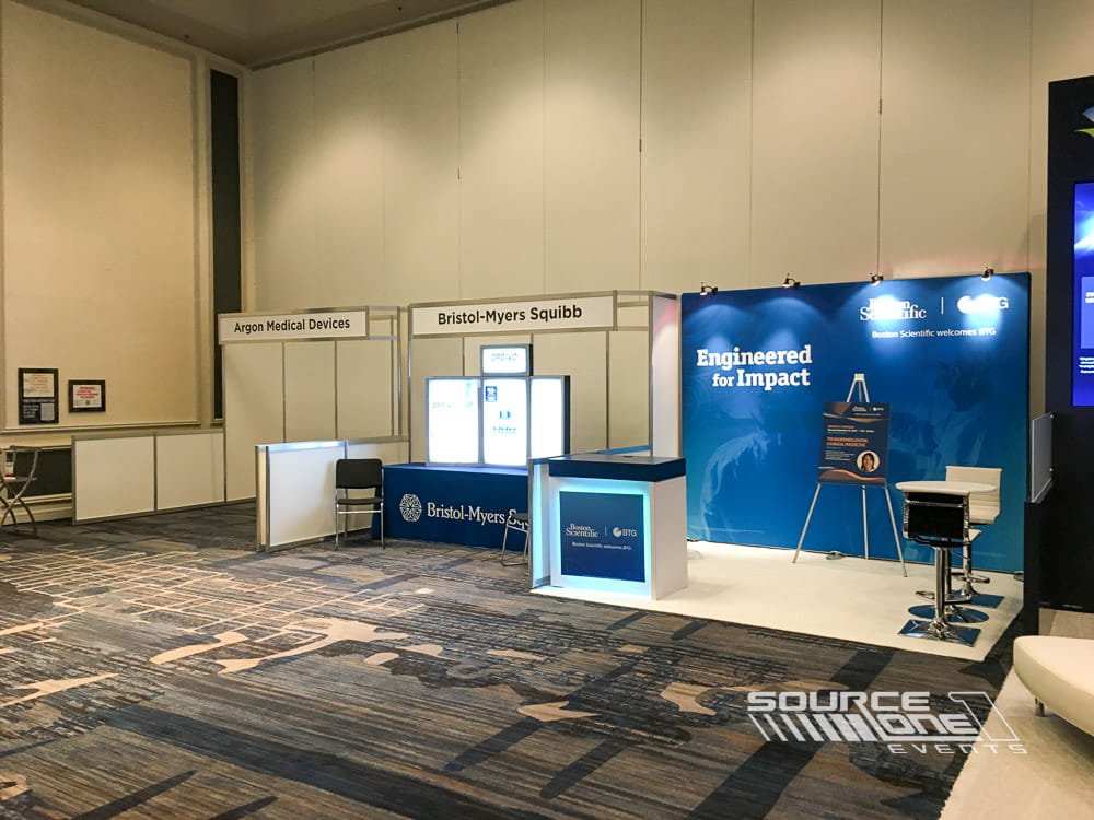 Custom hardwall trade show booth featuring blue branded graphics, digital displays, and integrated meeting space.
