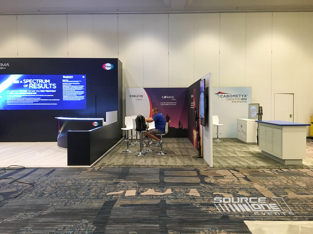 Large conference exhibit with blue branding, digital monitors, reception counter, and custom exhibit construction.
