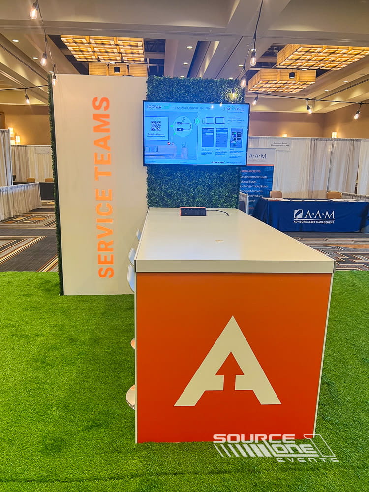 Custom branded information counter with digital displays and event graphics inside a convention center.