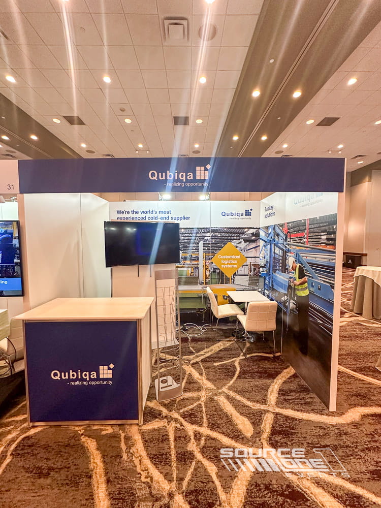 Contemporary custom trade show booth featuring warm wood finishes, white counters, overhead lighting, and branded exhibit graphics.