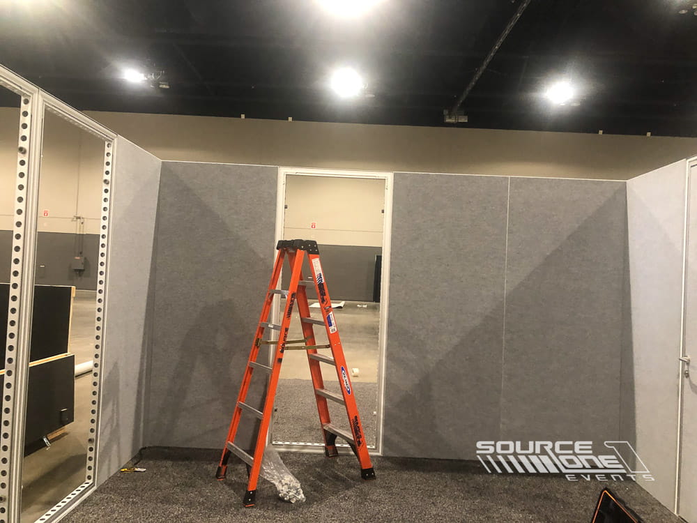 Modular hard-wall exhibit room under installation with ladder, demonstrating Source One Events' temporary room construction services.