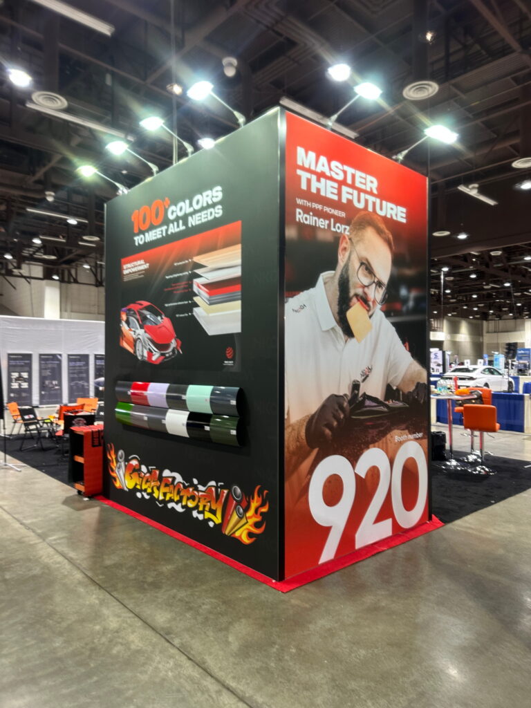 Automotive-themed trade show exhibit with oversized LED graphics, bold red branding, and custom experiential booth design.