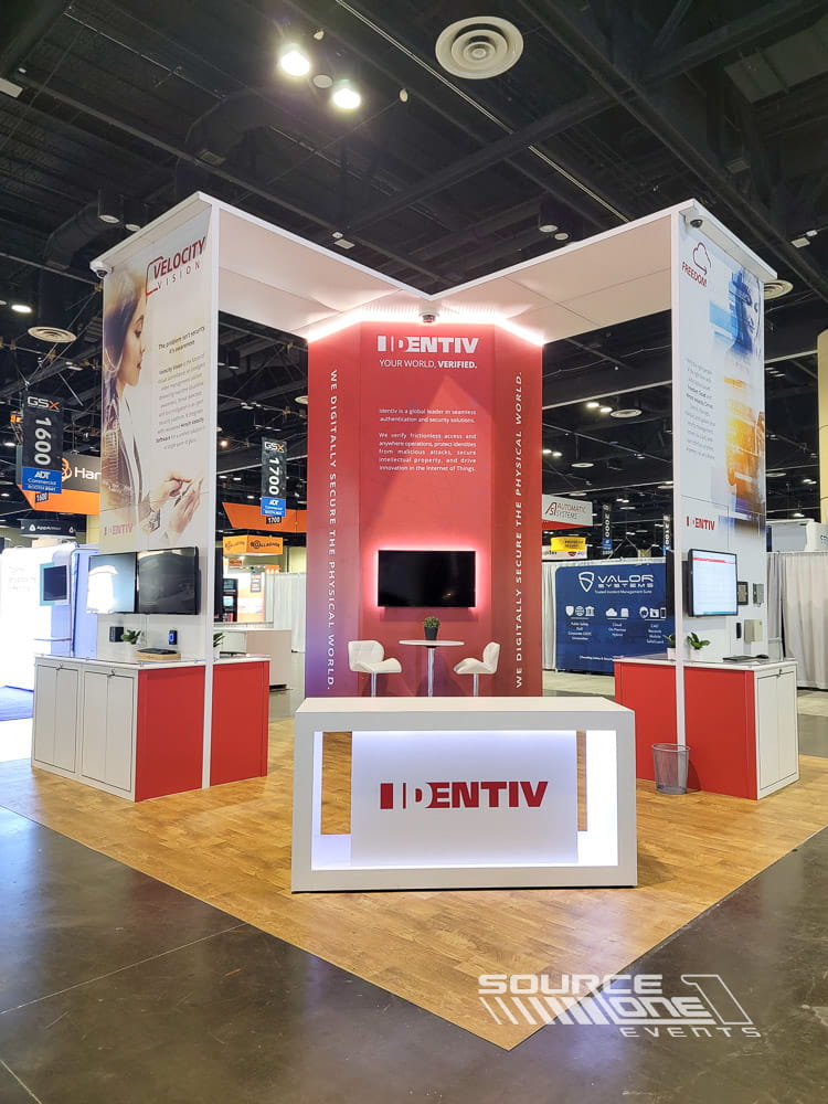 Contemporary island exhibit featuring vibrant red graphics, meeting spaces, digital displays, and custom architectural elements.