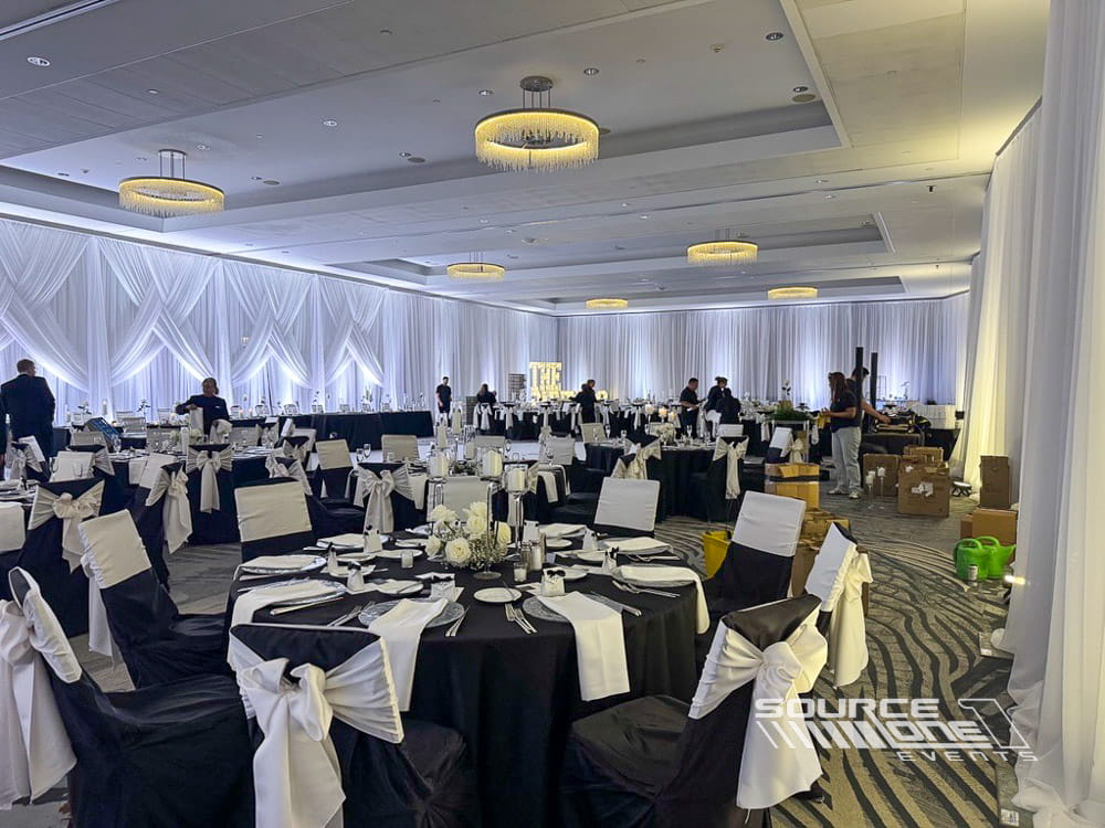 Elegant ballroom with white draped walls, round banquet tables, stage lighting, and custom event production for a formal corporate event.