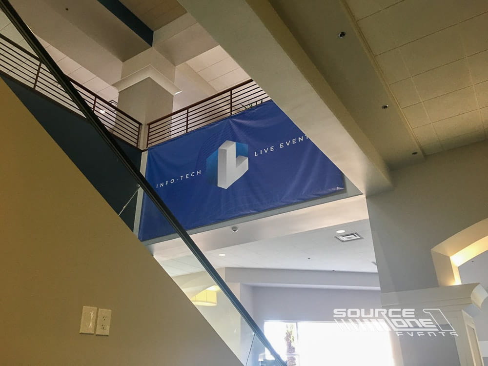 Blue hanging banner suspended above the exhibit floor providing exhibitor branding and attendee wayfinding.