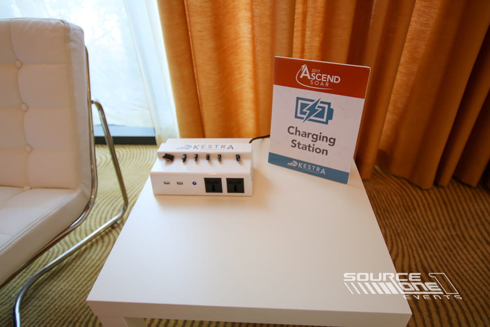 Portable charging kiosk with custom sponsor branding and charging capabilities positioned in a conference hallway.