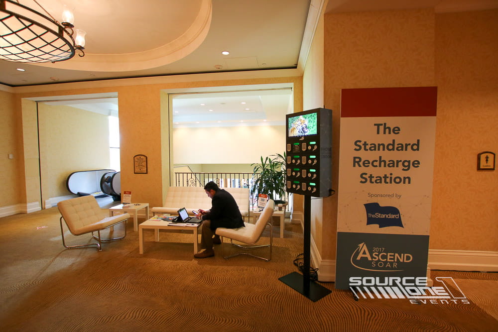 Freestanding mobile charging station with digital display, branded graphics, and convenient charging access for conference attendees.