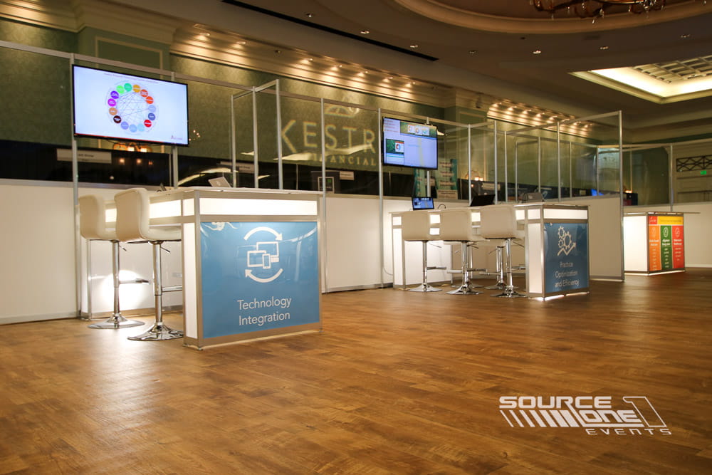 Modern exhibitor workstation with high-top counters, digital displays, and attendee consultation area.